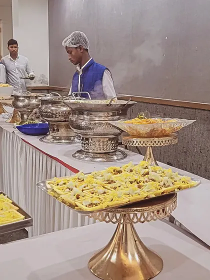 A staff member serving guests at a buffet. The setup includes elegant tiered serving platters for appetizers and silver chafing dishes for main courses.