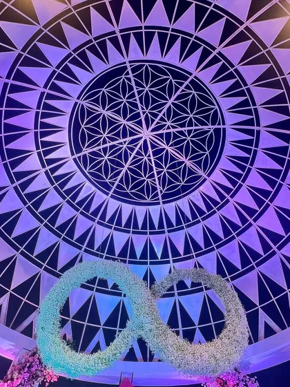 The ceiling of the 'Anant' dome, featuring the Flower of Life pattern, with the floral infinity symbol suspended below. This detail represents the couple's eternal journey beginning under a sacred sky.