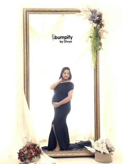 A creative and artistic portrait using a large, ornate mirror frame. The mom-to-be in a classic black gown is perfectly framed, creating a picture within a picture.