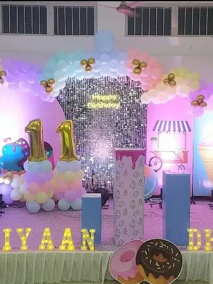 A donut and ice cream themed "Sweet 1" birthday party. The stage is decorated in pastel colors with a shimmer wall and large marquee letters for the names.