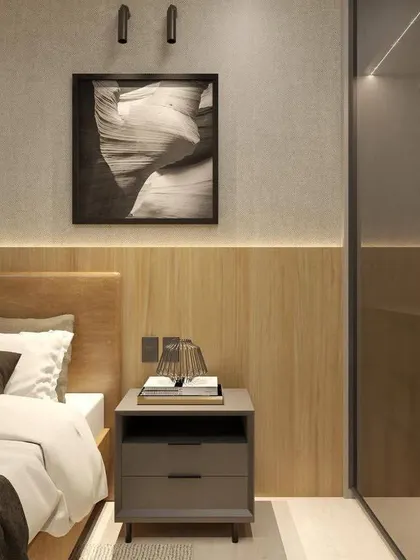 A close-up of a bedside setup in a modern bedroom. The design includes a wooden headboard, a minimalist side table, and a contemporary wall lamp.