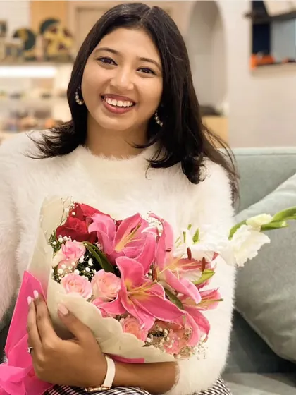 A warm smile from our founder, holding a beautiful bouquet of pink lilies and roses. This is a look behind the brand, showing the passion and person dedicated to gifting smiles and creating magic.