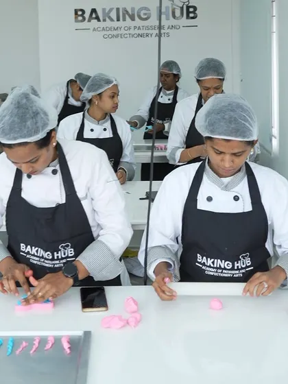 Teamwork in action. Students work together at a station, rolling and shaping fondant decorations. Our classes foster a sense of community and shared learning.