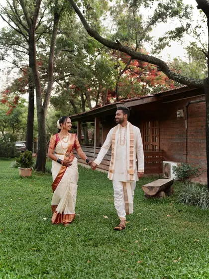 A happy couple walking hand-in-hand. The bride's makeup is designed to look natural yet elegant, perfect for an outdoor wedding setting.
