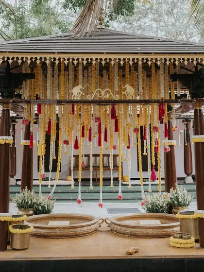 The Haldi mandap is decorated with hanging strings of white and yellow flowers, along with colorful tassels, creating a festive and playful look.