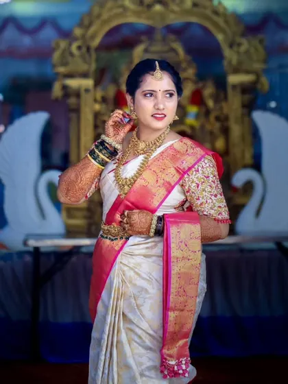 This bride looks absolutely regal. Her makeup features a classic combination of gold eyeshadow and a bold pink lip, which beautifully matches her white and pink Kanchivaram saree.