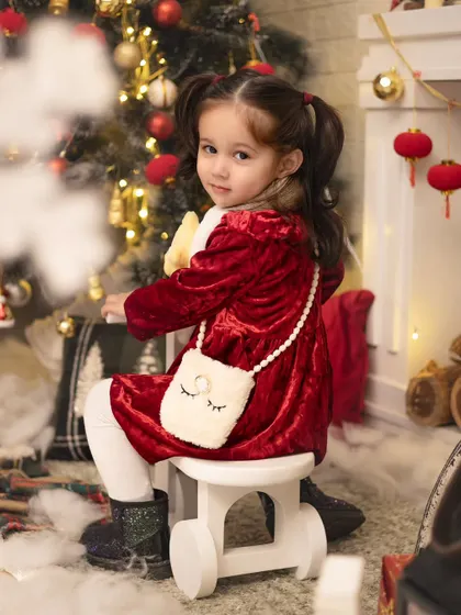 A little girl in a red velvet dress, looking like a Christmas doll. Our festive sessions include beautiful outfits to complete the holiday look.