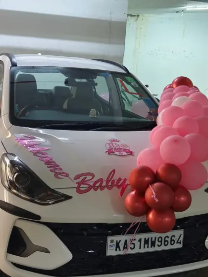 The complete car decoration for a baby girl's homecoming. A garland of pink and red balloons on the hood and "Welcome Baby" vinyl lettering ensure she arrives in style.