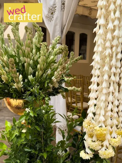 Fresh tuberose stalks in a golden vase next to a hanging garland, highlighting the use of fragrant flowers in traditional setups.