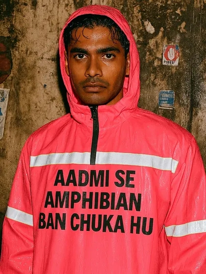 A man in a pink raincoat that says 'AADMI SE AMPHIBIAN BAN CHUKA HU'. This 'Rainquotes' piece humorously describes the feeling of evolving to survive the annual city floods.