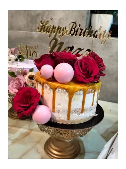 A stunning birthday cake featuring a caramel drip, fresh red roses, and pink chocolate spheres. The combination of colors and textures is just beautiful.