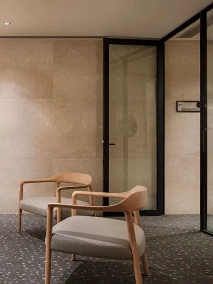 A quiet seating nook within the Elevate Clubhouse. The use of natural stone walls, terrazzo flooring, and minimalist wooden chairs creates a serene corner for relaxation or informal conversation.