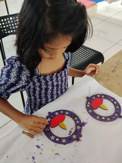 A young artist is focused on creating a decorative wall hanging with a diya design for Diwali.