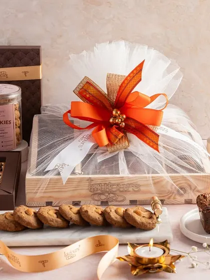 A cozy and indulgent Diwali hamper featuring a loaf cake, a wrapped gift crate, cookie jars, and boxes of brownies. This collection is perfect for a family to share and enjoy during the holiday.