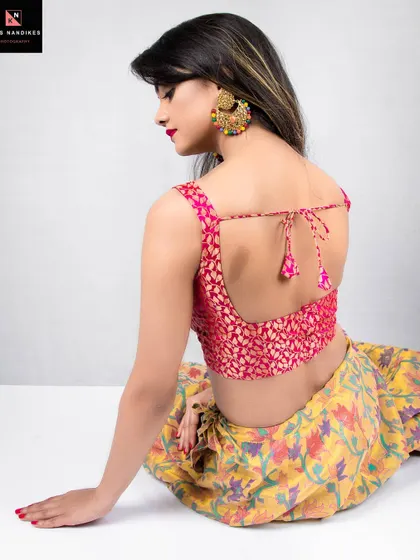 A view from the back of a model sitting in a traditional lehenga. This shot highlights the colorful skirt and the design of the backless blouse, capturing a moment of quiet grace.