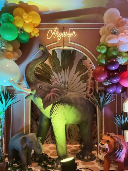 This jungle backdrop features a magnificent elephant prop, the birthday boy's name in neon, and lush green and brown balloons.