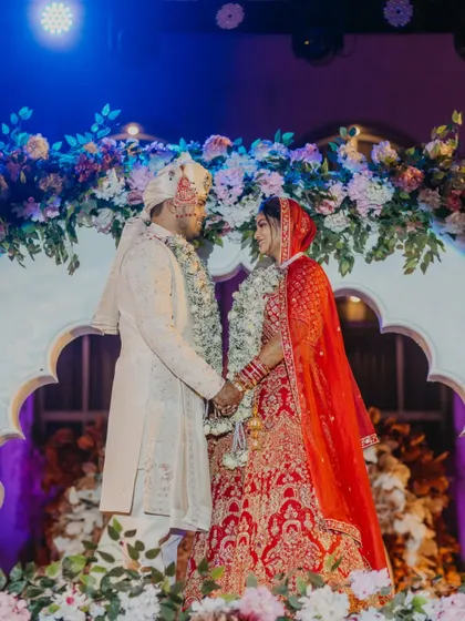 A full-length shot of the couple on their beautifully decorated wedding stage. The lighting and floral decor create a stunning backdrop for this timeless portrait.