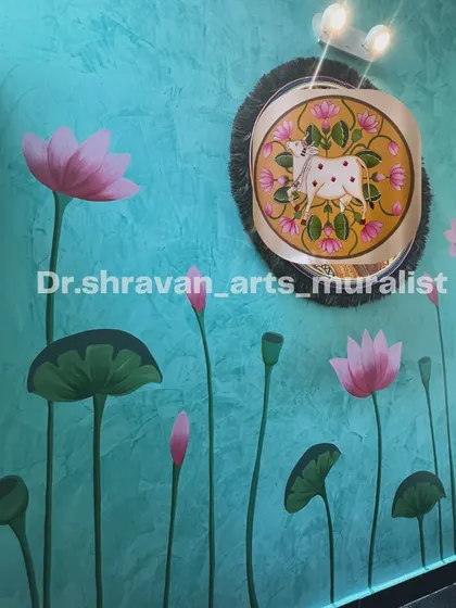 This mural combines a textured turquoise background with a Pichwai-style painting. The main subject is a miniature Pichwai painting of a cow, surrounded by large, elegant lotus stems.