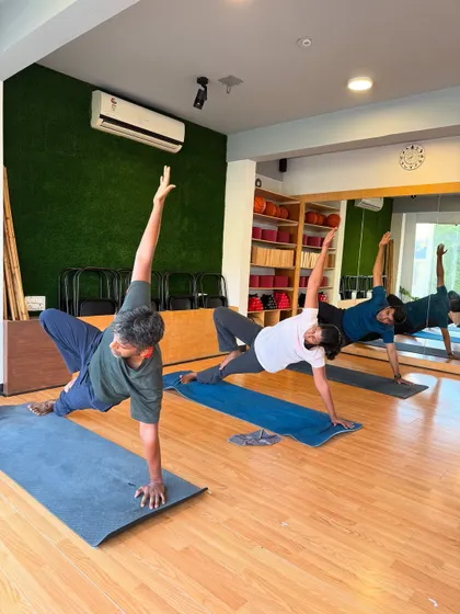 Students hold a strong side plank, building core and shoulder strength. The mirror reflects the collective effort of the class.
