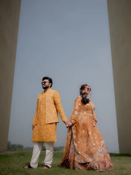 A stylish portrait of the couple holding hands after their Haldi ceremony, looking cool and happy in their matching yellow outfits.
