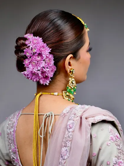 A classic for a reason. This elegant twisted bun, adorned with a cascade of fresh purple chrysanthemums, is a timeless choice for the main wedding day. It’s structured to hold the dupatta securely and stay perfect through all the ceremonies.