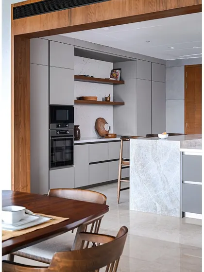 A view from the dining area into the sleek, modern kitchen. The wooden frame around the kitchen entrance defines the space while maintaining the open feel.