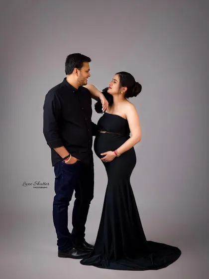 A sweet and classic pose for a maternity shoot. The couple's coordinated black outfits and the simple backdrop result in a clean and timeless portrait.