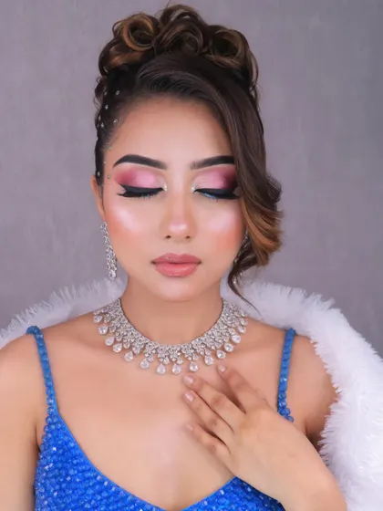 A stunning party look in a sequined blue dress, featuring creative pink and blue eye makeup and a messy high bun.