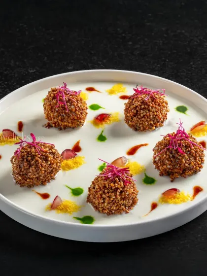 Dahi ke kebab, yogurt patties, fried and served on a bed of cream with colorful sauce droplets.