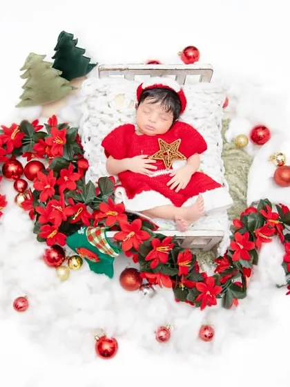 A Christmas angel sleeping on a bed of clouds. Dressed in a festive red outfit and surrounded by poinsettias, this baby is the perfect holiday star.