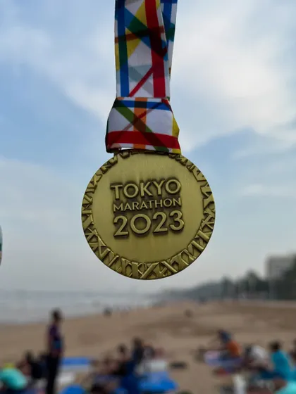 The 2023 Tokyo Marathon medal, held up against the backdrop of our Juhu beach training ground. We bring world-class goals to our local community.