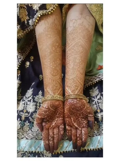 A full view of the final bridal mehendi stain. This showcases how the design flows from the hands up the arms, with a consistent and rich color payoff.