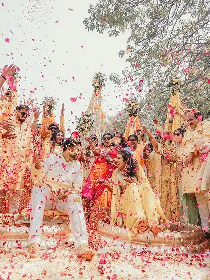 A wide-angle shot capturing the scale of the Haldi celebration, with all the guests participating in showering the couple with love and petals.