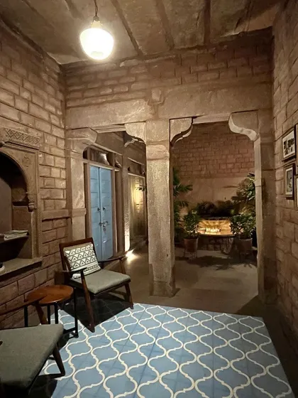 This cozy reading nook in a Jodhpur heritage hotel shows how to blend textures and patterns. The stone pillars, patterned floor tiles, and simple wooden furniture create a space that feels both historic and welcoming, a great reference for creating inviting corners at home.