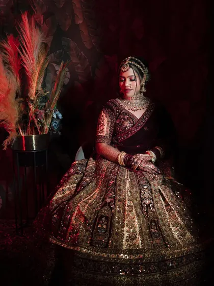 A wider version of the regal seated portrait, showing more of the opulent lehenga and the artistic, dark setting.