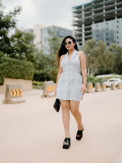 A full-length shot of a model walking in a stylish dress. The urban background and her confident stride create a classic fashion-on-the-move image.