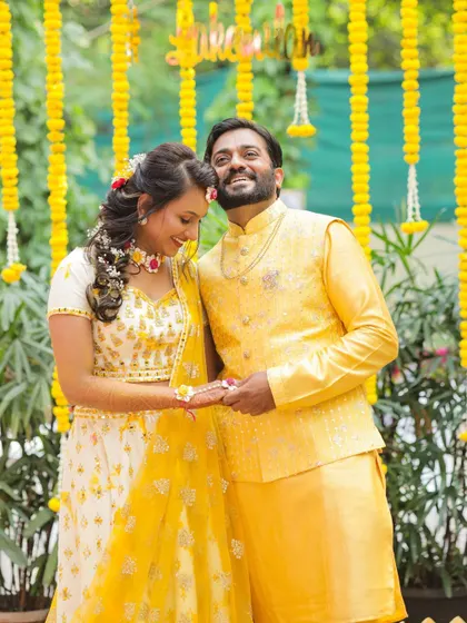 A happy portrait of the couple against a backdrop of marigold flowers. The vibrant yellow decor is a hallmark of a fun Haldi ceremony.