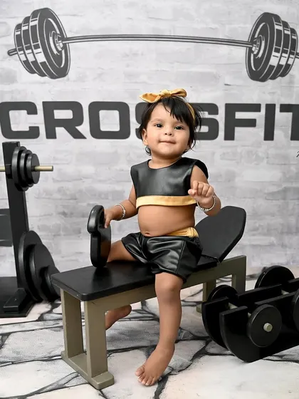 Getting her reps in early! This little girl is all business in her CrossFit-themed photoshoot, sitting on a miniature workout bench. It's a fun and strong theme for a baby girl.