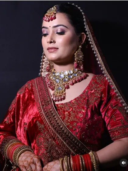 A close-up of a bride in a red velvet lehenga, focusing on the intricate jewellery and the rich texture of the embroidered fabric.