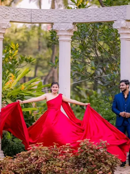 The woman takes center stage, showcasing her flowing red gown against the classic white pillars. This pose creates a beautiful, dynamic shape and highlights the elegance of the outfit.