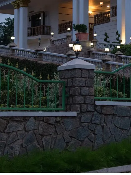 A detail of the stonework and custom metal railing at 'The Palace Promised'. The combination of rough-hewn stone walls and ornate green fencing is a key part of the classical landscape design.