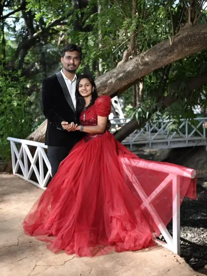 A romantic photo on a picturesque bridge. The bride's red ball gown stands out beautifully against the lush green background of the park.