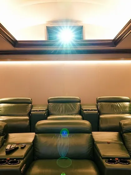 The projector light illuminates the front rows of this classic theater, highlighting the rich color of the leather seats and the warm, ambient cove lighting in the ceiling.
