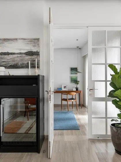 A peek into a study from the hallway. The clean white walls, minimalist furniture, and a large fiddle-leaf fig plant create a space that is bright, calm, and conducive to focus.
