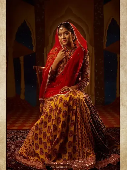 The character of Dasi Kamini, the handmaiden. Her block-printed lehenga and simple red veil are styled to be authentic to her station, yet with a grace that hints at her own story within the palace.