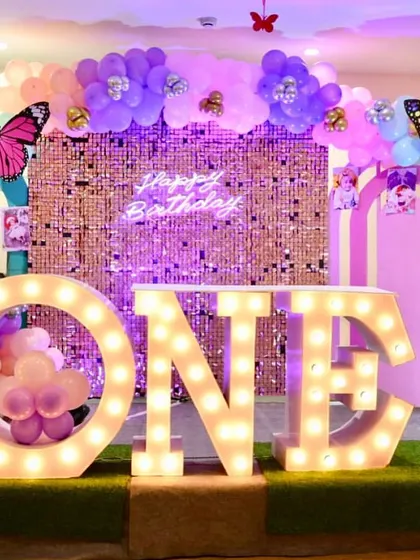 A grand first birthday celebration with a butterfly theme. The large marquee letters, sequin backdrop, and colorful balloon arch create a stunning visual impact.