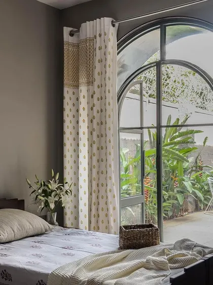 A guest bedroom with a large arched window that opens directly onto a patio. The design prioritizes light and air, creating a bright and welcoming space for visitors.