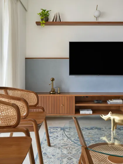 A detailed shot of the 'Malhar' living room, focusing on the custom TV unit with a textured blue-grey backdrop. The clean lines and natural wood tones are central to the contemporary classical theme of the home.