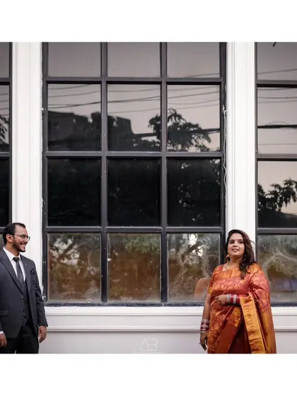 A black and white portrait of a couple standing before a large window. The distance between them creates a sense of anticipation and quiet connection.