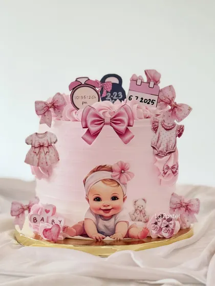 The sweetest cake to welcome a new baby girl. This pink cake is adorned with edible illustrations of baby clothes, bows, a calendar with the birth date, and a clock showing the time of birth.